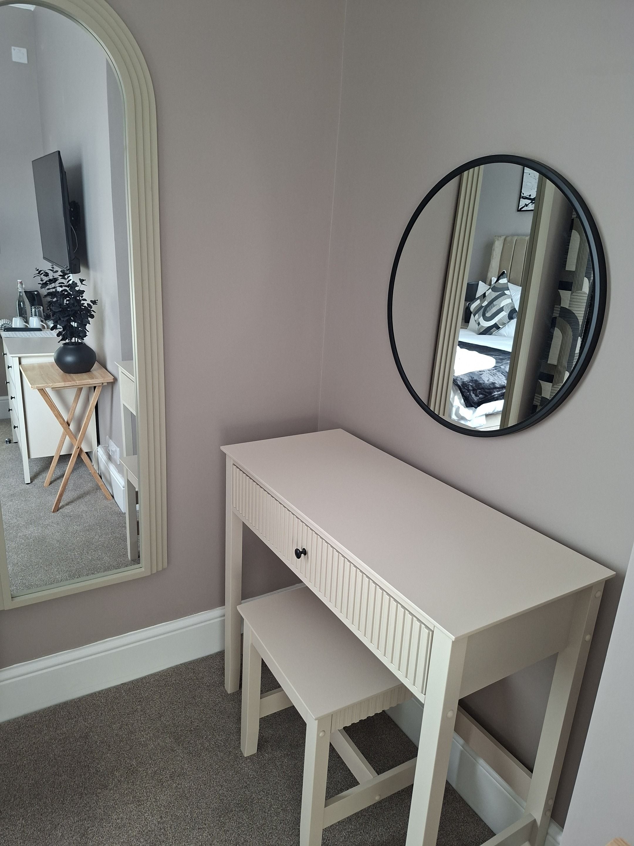 A room with a white desk, a mirror, and a small stool.