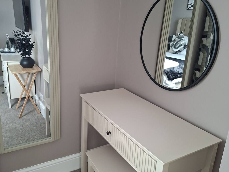 A room with a white desk, a mirror, and a small stool.