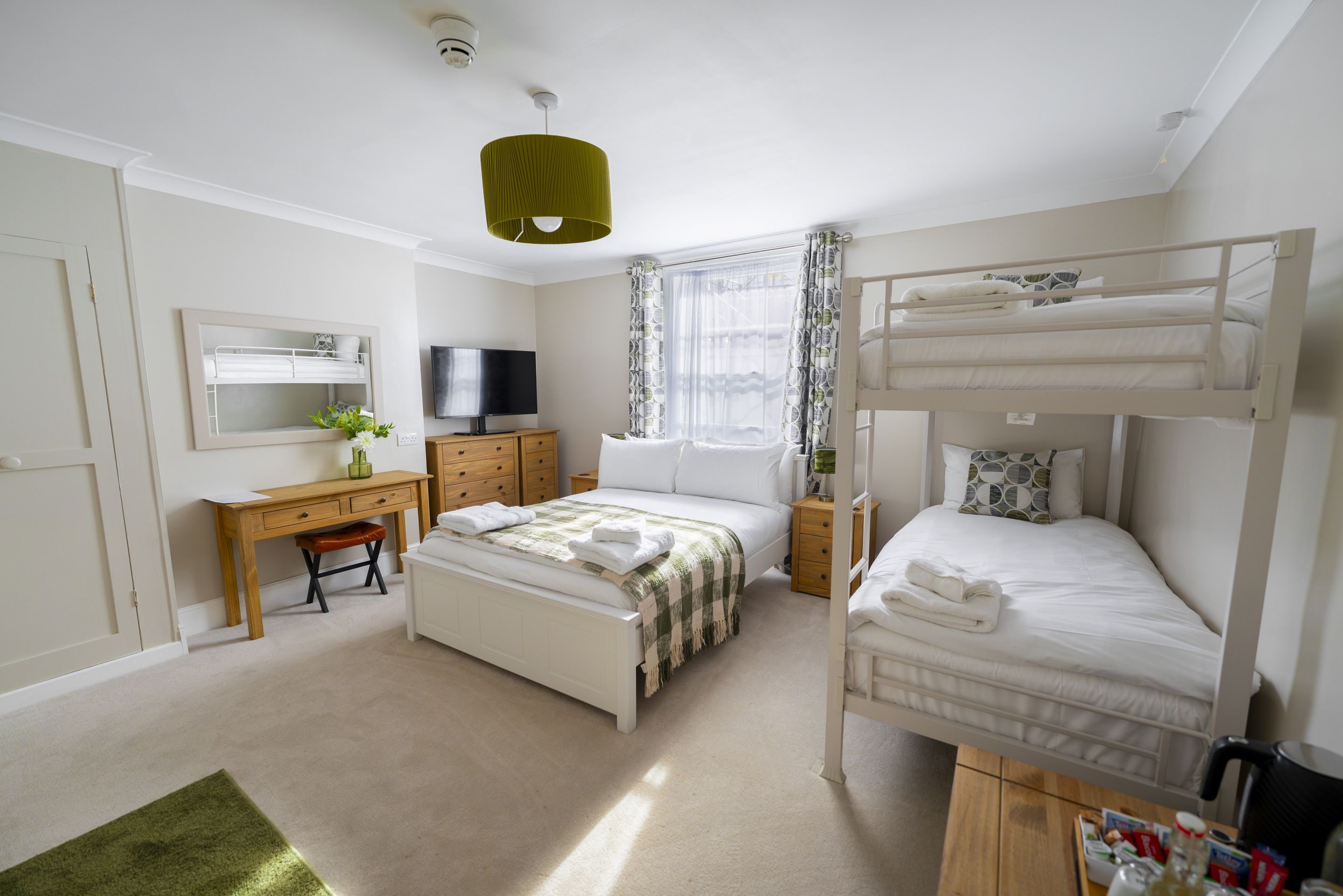 A bedroom with bunk beds, a desk, a television, and a window with curtains.