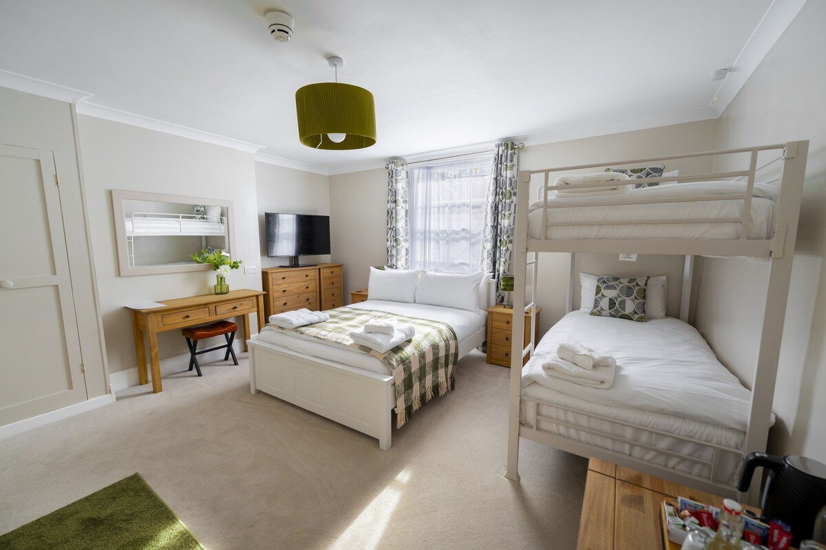A bedroom with bunk beds, a desk, a television, and a window with curtains.