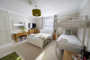 A bedroom with bunk beds, a desk, a television, and a window with curtains.