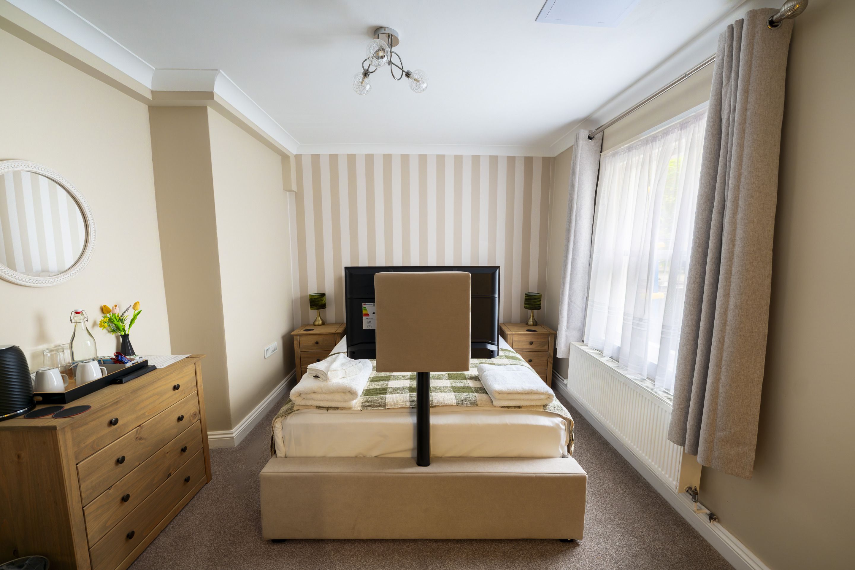 Una camera d'albergo con un letto, una scrivania, una sedia, un televisore e una finestra con tende.
