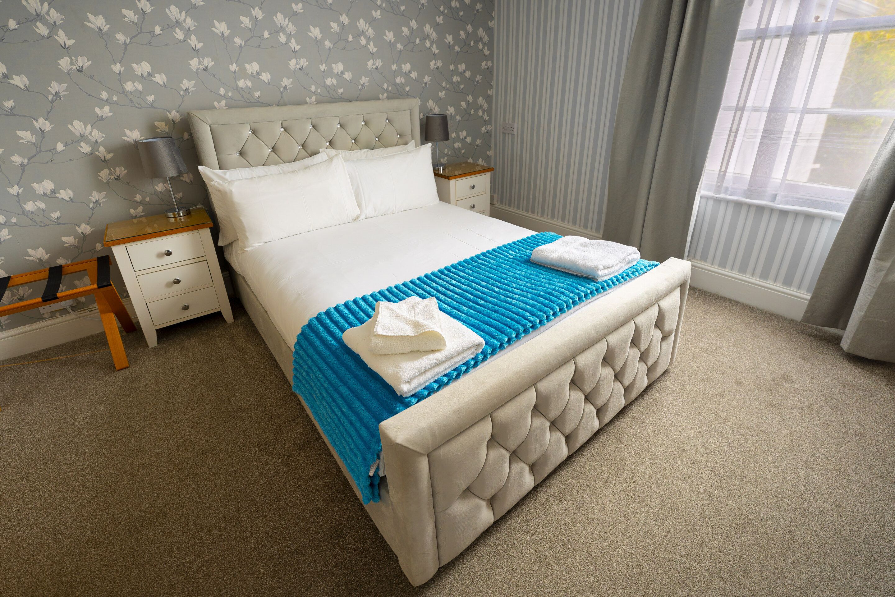 A neatly made bed with a blue and white striped blanket, a tufted headboard, and white bedding.