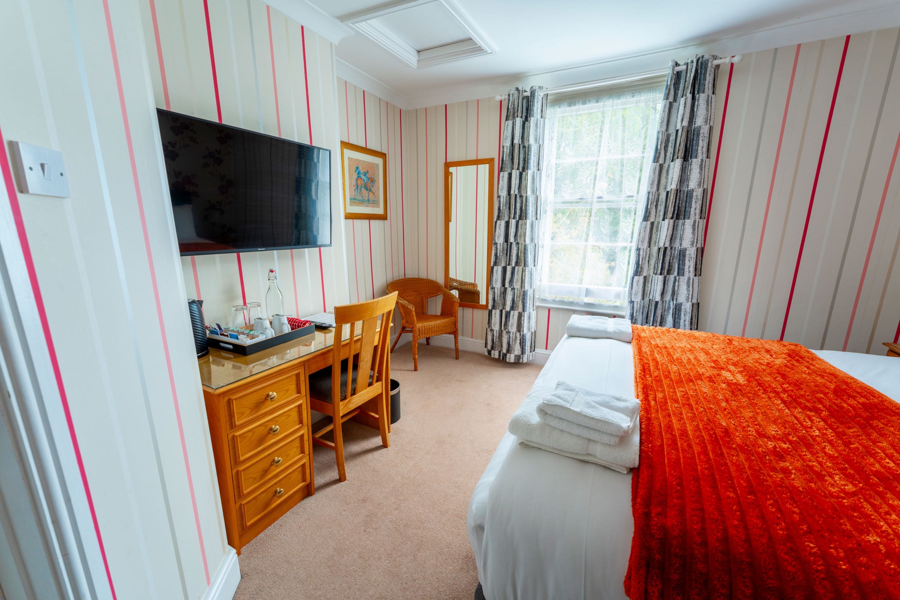 A hotel room with a bed, a desk, a chair, a television, and a window with curtains.