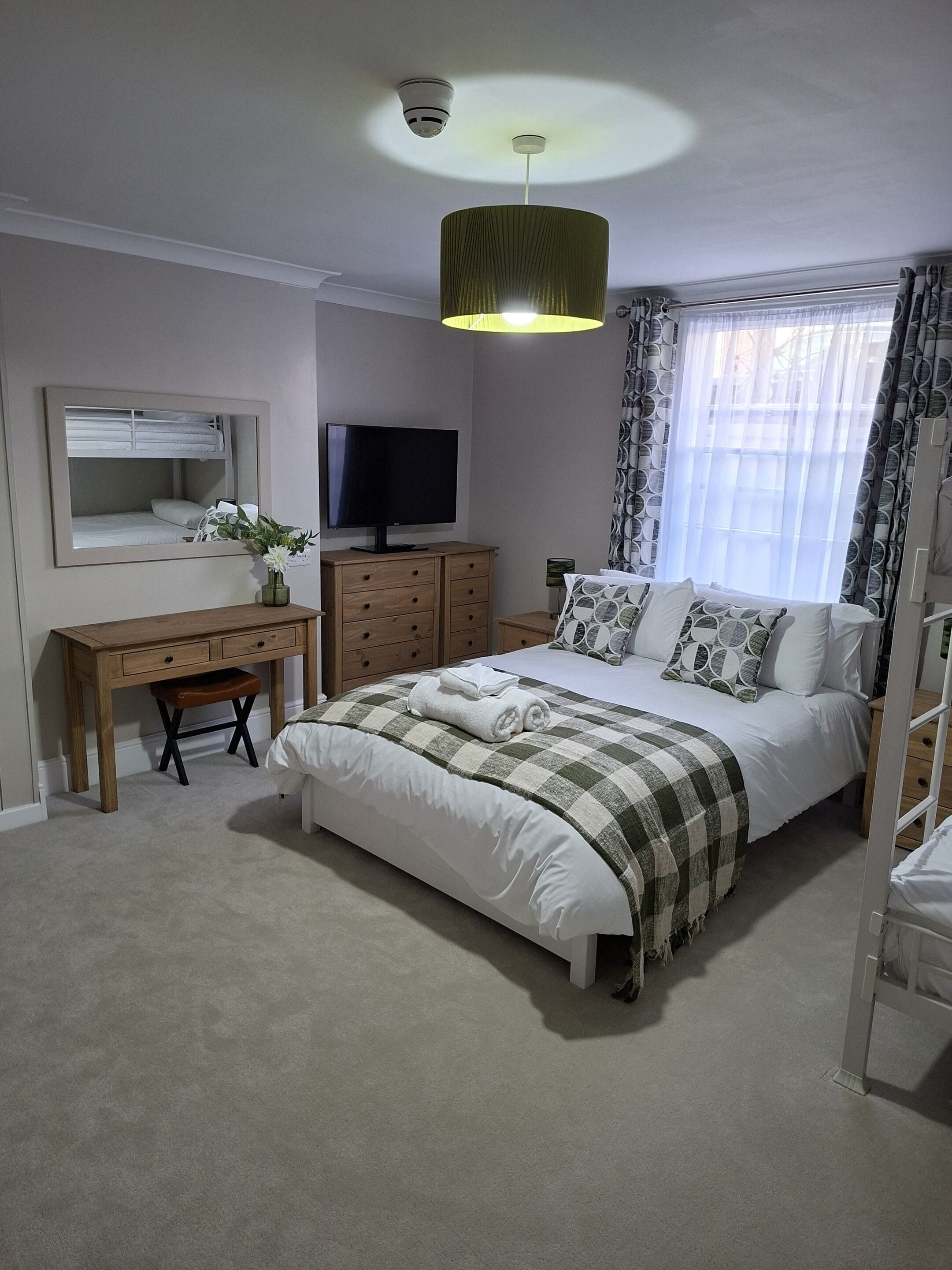 A bedroom with a bed, a desk, a television, and a window with curtains.