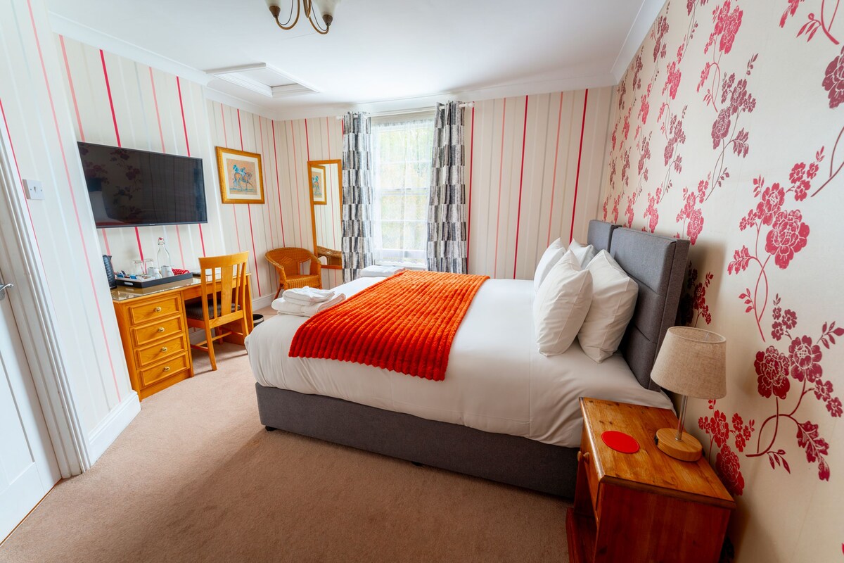 A bedroom with a bed, a desk, a chair, a television, and a window with curtains.