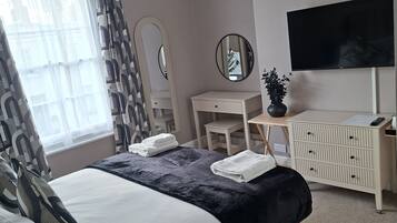 Un dormitorio con cama, mesitas de noche, cómoda, televisor y ventana con cortinas.