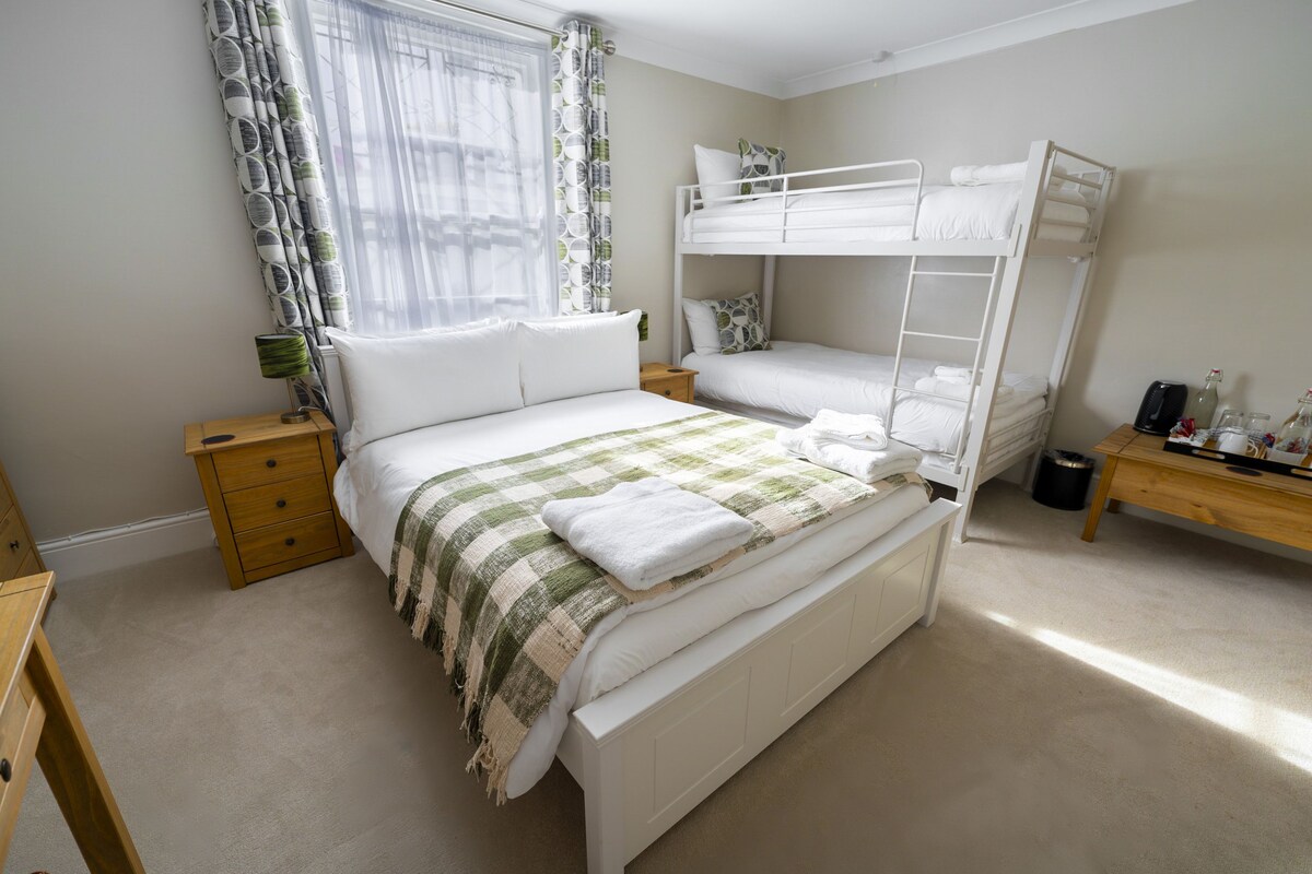 Een slaapkamer met een stapelbed, een nachtkastje met een lamp en een raam met gordijnen.