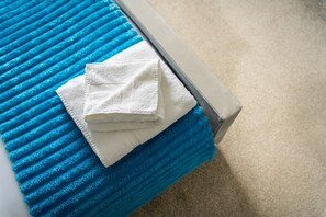 A bed with a blue textured cover and a white towel on it.