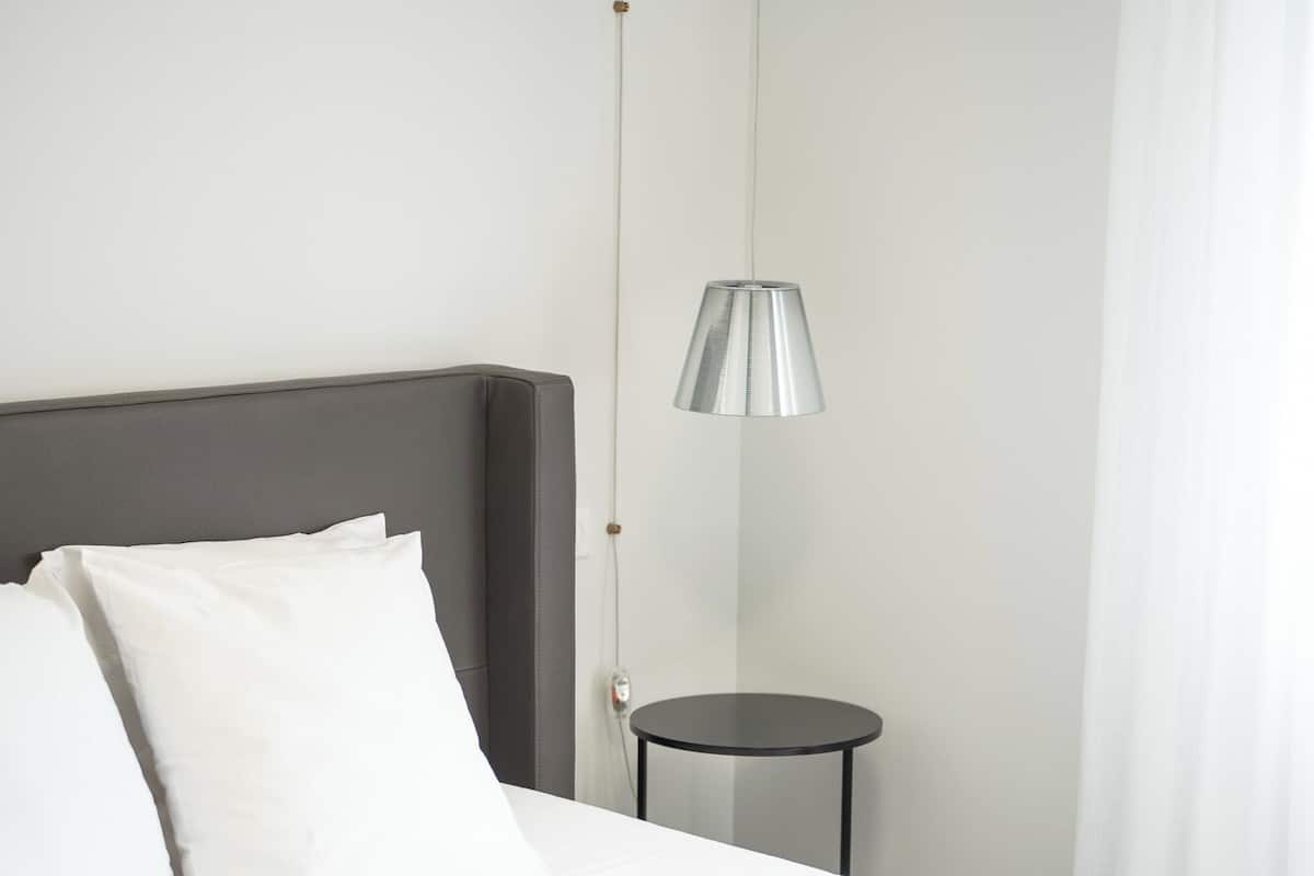 A hotel room with a bed, a bedside table, a lamp, and a window with curtains.