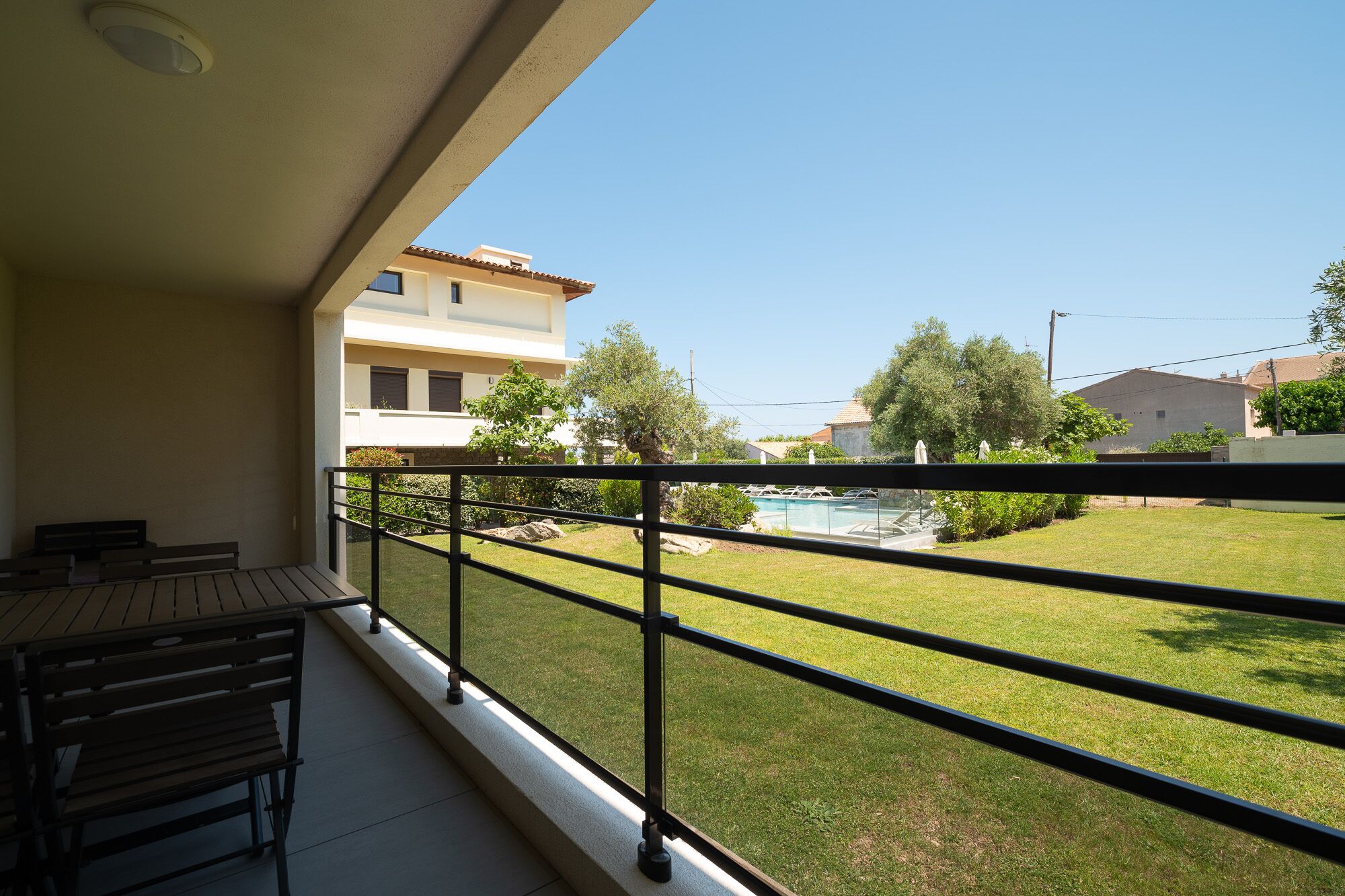 A balcony with a metal railing overlooking a swimming pool and a grassy area with trees.