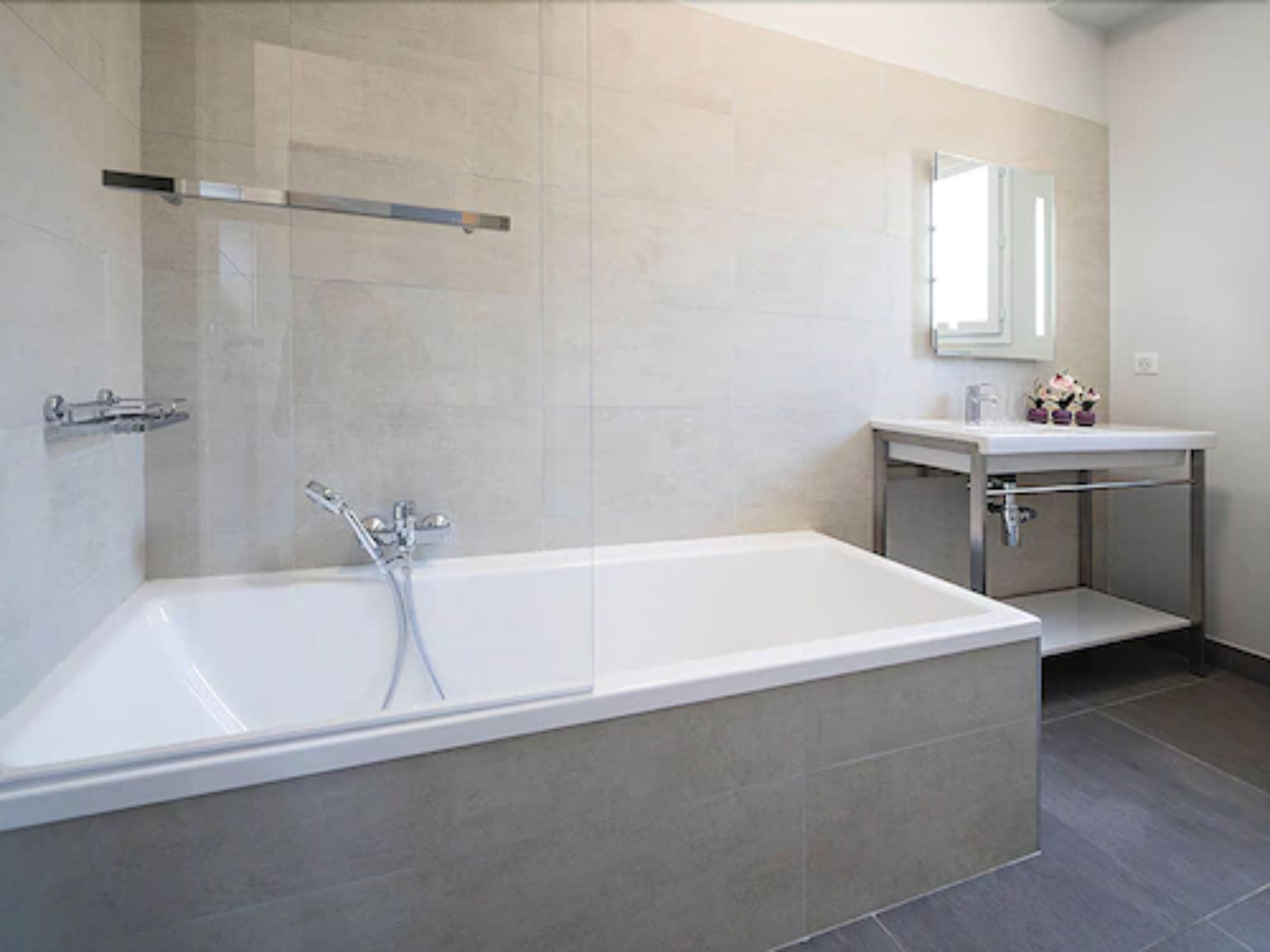 Un baño moderno con una bañera independiente, un tocador con espejo y paredes cubiertas de azulejos.