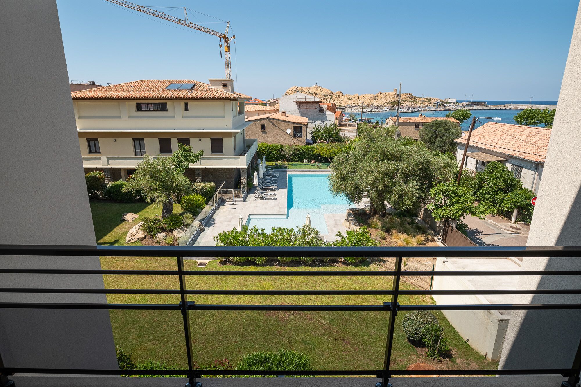A residential area with a swimming pool, a view of the sea, and a construction crane in the background.