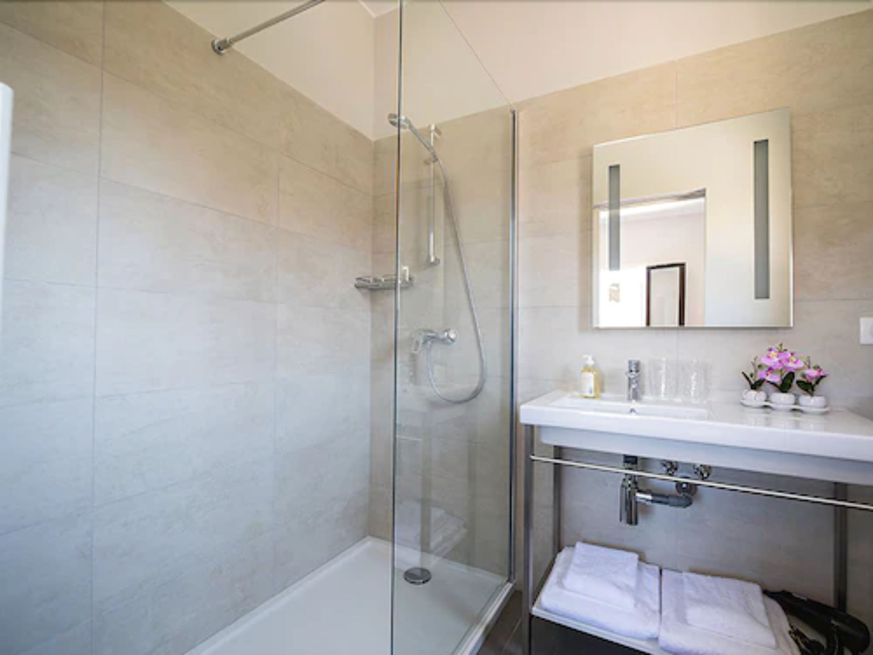 A modern bathroom with a glass-enclosed shower, a white sink, and a mirror above it.