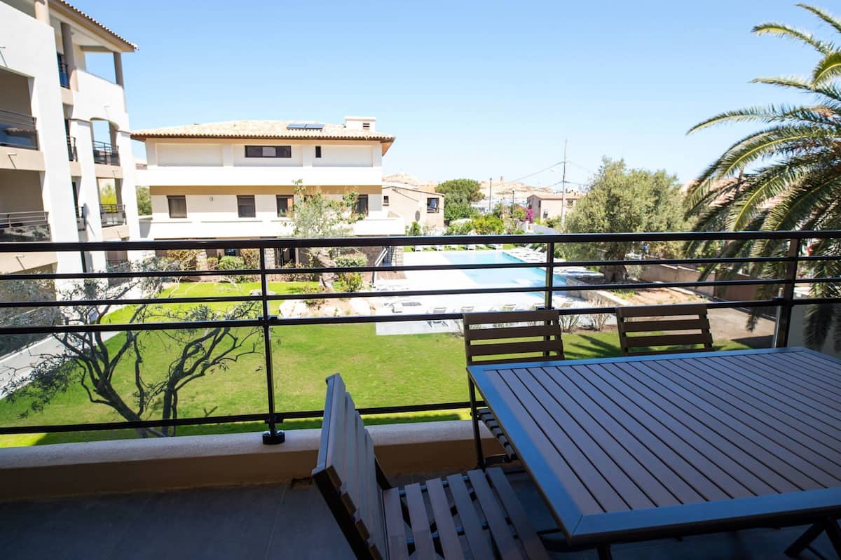 A balcony with a view of a swimming pool, a grassy area, and a building with multiple floors.