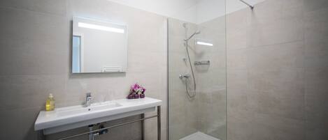 A modern bathroom with a glass shower enclosure, a white sink with a mirror, and a shelf with towels.
