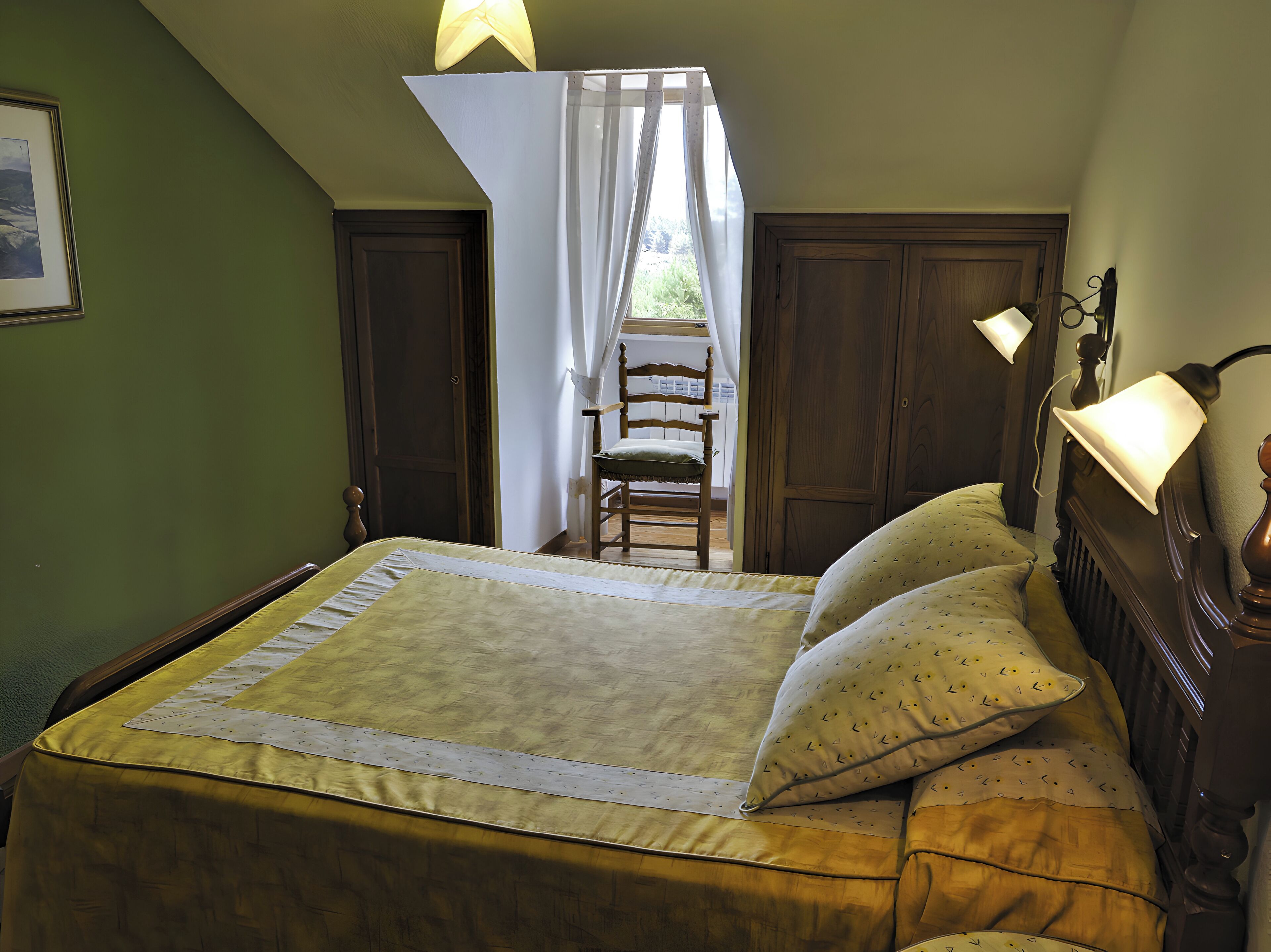 Un dormitorio con cama, una silla, un ventanal con cortinas y una lámpara.