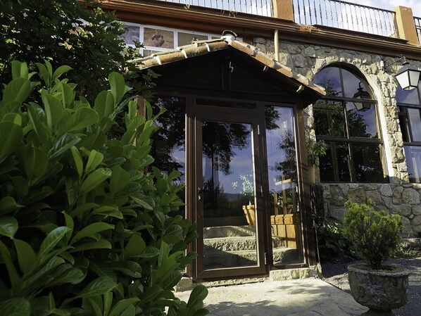 A stone building with a covered entrance, large windows, and a small garden area. - Hospedium Hostal Almanzor (Navarredonda de Gredos)