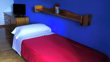 Um quarto com uma cama, uma televisão sobre um aparador, uma prateleira de madeira com um vaso e uma parede azul.