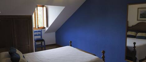 A bedroom with a sloped ceiling, a bed with a wooden headboard, a chair, a desk, and a window with natural light.