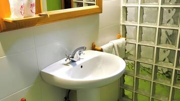 Een badkamer met een wit wastafel, houten handdoekhouder en een douchegedeelte betegeld met groene tegels.
