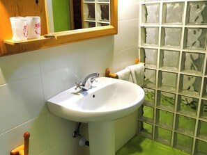 Un baño con lavamanos blanco, toallero de madera y zona de ducha con azulejos verdes.