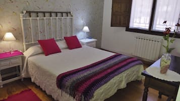 Un dormitorio con cama, dos mesitas de noche con lámparas, un radiador, una ventana con cortinas y una alfombra roja.