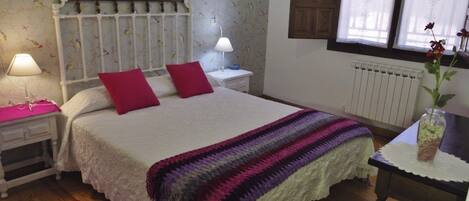 A bedroom with a bed, two bedside tables with lamps, a radiator, a window with curtains, and a red rug.