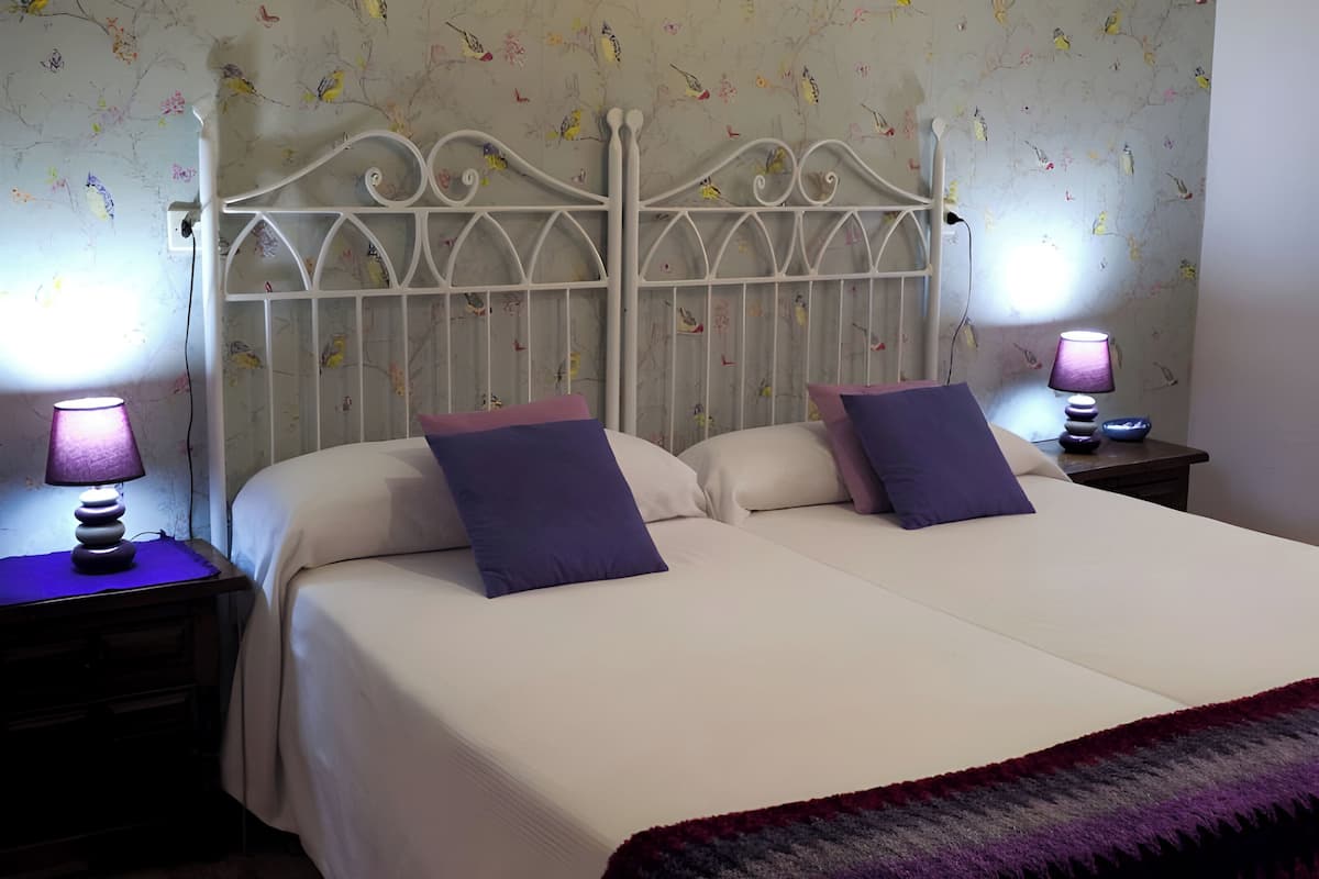 Un lit double avec une tête de lit blanche et deux tables de chevet, chacune équipée d’une lampe.