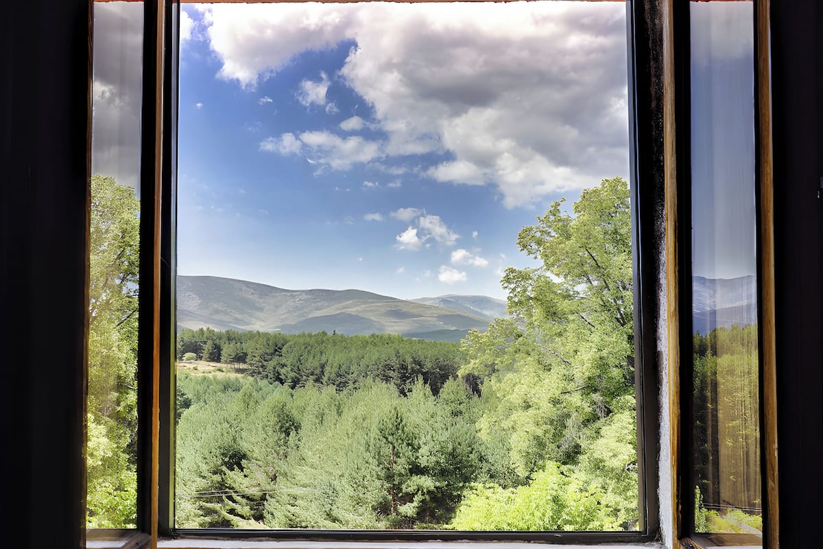 Une fenêtre donnant sur un paysage boisé et des montagnes.