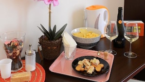 Une table à manger avec un bol de macaronis, une assiette de nourriture, une bouteille de vin et une plante en pot.
