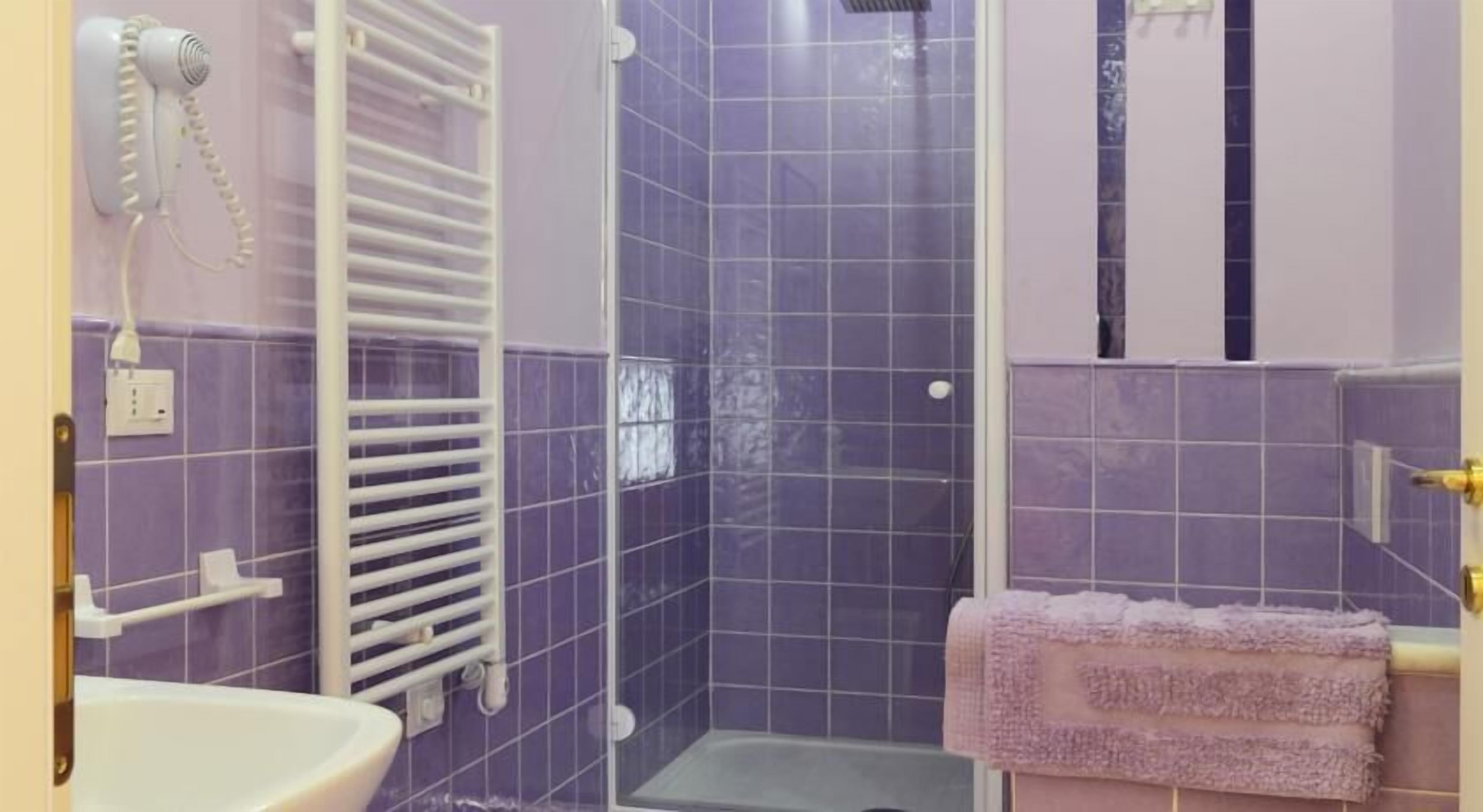 A bathroom with purple tiles, a white sink, a towel rack, and a shower area.