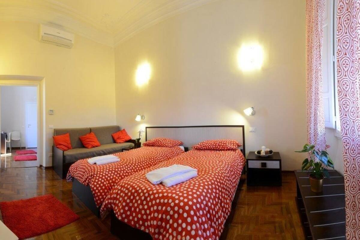 A bedroom with two beds, a sofa, a small table, and a potted plant.