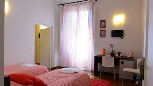 Une chambre avec deux lits, un bureau, une chaise, une télévision et une fenêtre avec des rideaux.