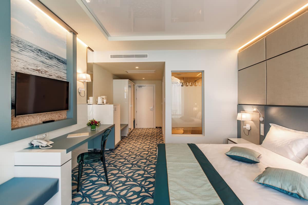 A modern hotel room with a bed, desk, chair, and a television.