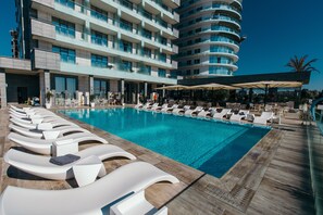 A poolside area with lounge chairs and umbrellas, a modern building with balconies, and a clear blue sky. - Hotel Opera (Navodari)