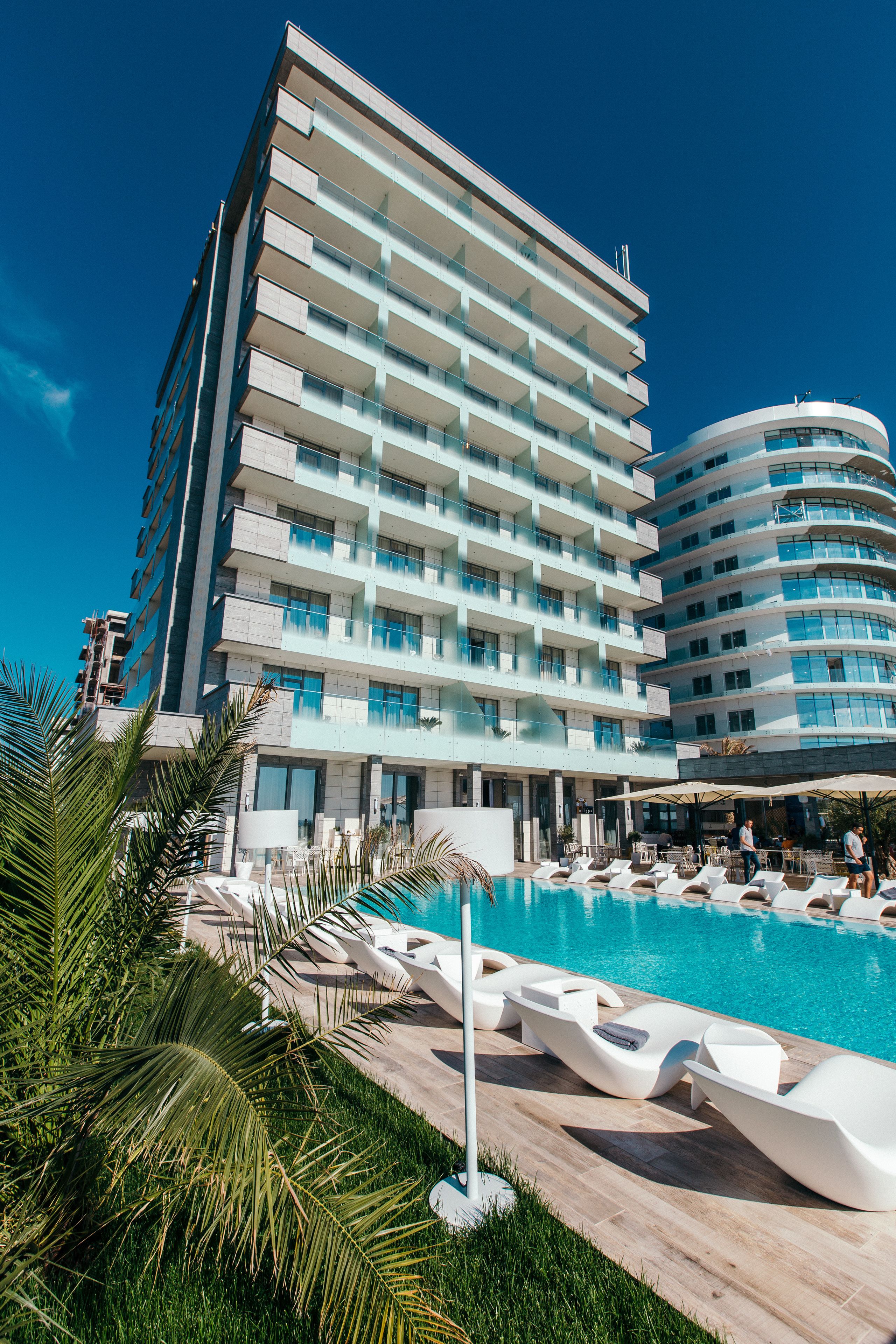 Un hôtel moderne doté d’un espace piscine comprenant des chaises longues et une piscine à l’eau d’un bleu cristallin.