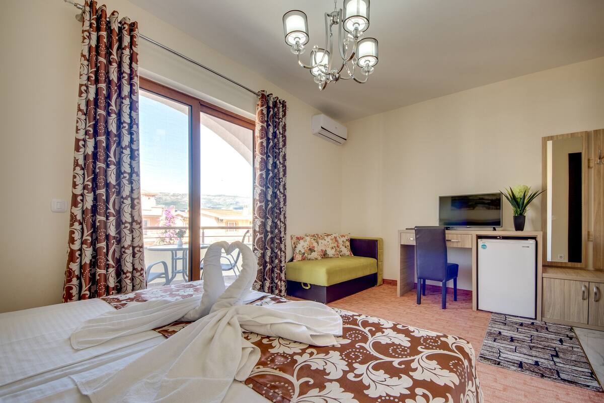 Una habitación de hotel con una cama, un escritorio, una silla, un televisor y un refrigerador pequeño.