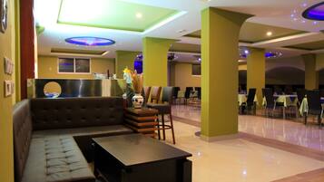A modern hotel lobby with a seating area, a reception desk, and a dining section.