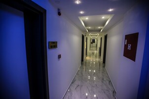 Un pasillo de hotel con piso de mármol, un cartel con la ubicación e un detector de incendios en la pared.