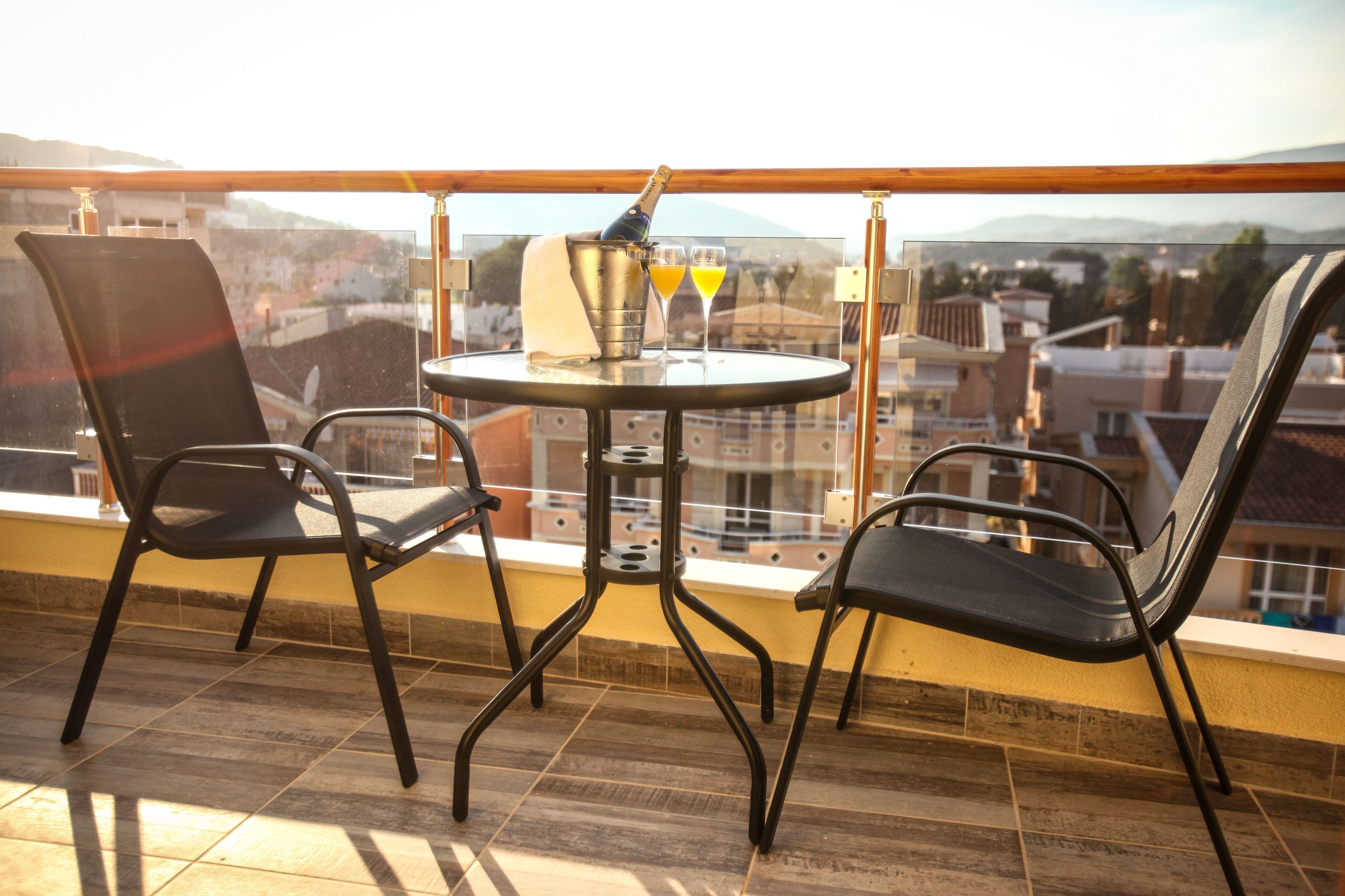 A balcony with two chairs and a table, a bottle of champagne, and two glasses of orange juice.