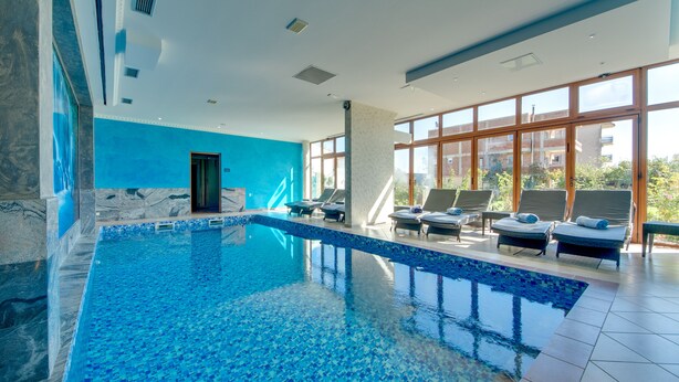 A modern indoor swimming pool with clear blue water, sun loungers, and large windows offering views of the surrounding area. - Hotel Montefila (Ulcinj)
