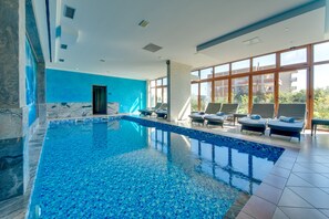 A modern indoor swimming pool with clear blue water, sun loungers, and large windows offering views of the surrounding area. - Hotel Montefila (Ulcinj)