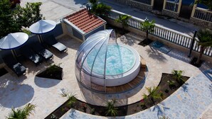 A rooftop pool with a glass enclosure, surrounded by lounge chairs and umbrellas, and a stone-tiled deck with palm trees. - Hotel Montefila (Ulcinj)