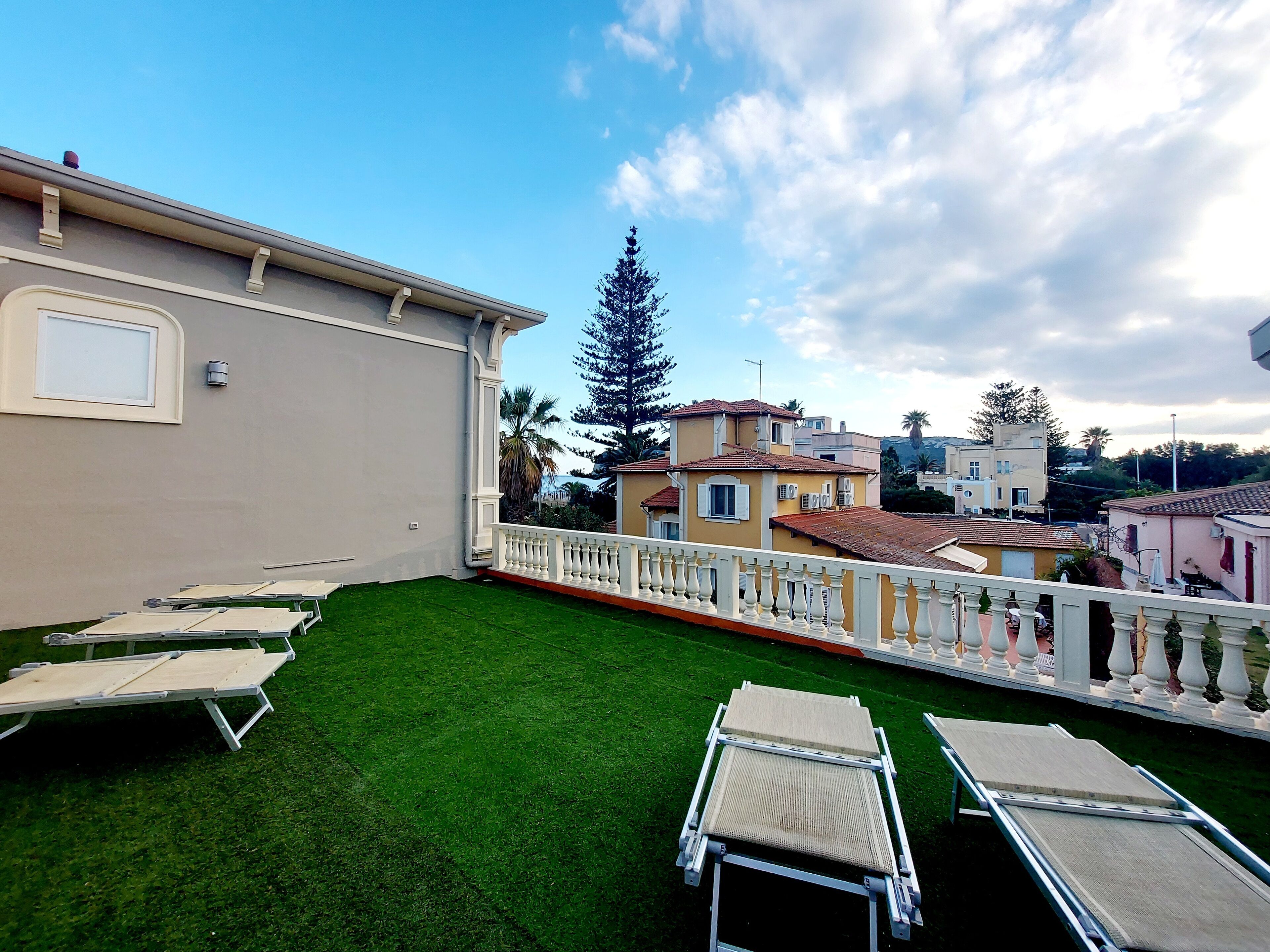 A rooftop terrace with artificial grass, white lounge chairs, and a white balustrade.