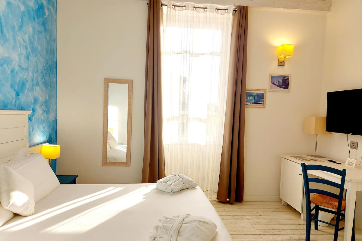 Hotellihuone, jossa on sänky, työpöytä, tuoli, televisio ja ikkuna, jossa on verhot.