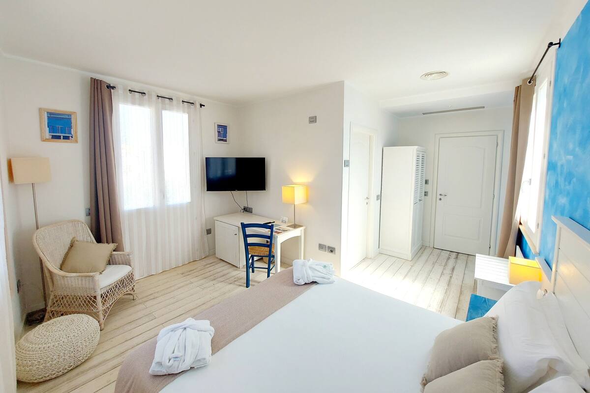 Hotellihuone, jossa on sänky, työpöytä tuolilla, televisio ja vaatekaappi.