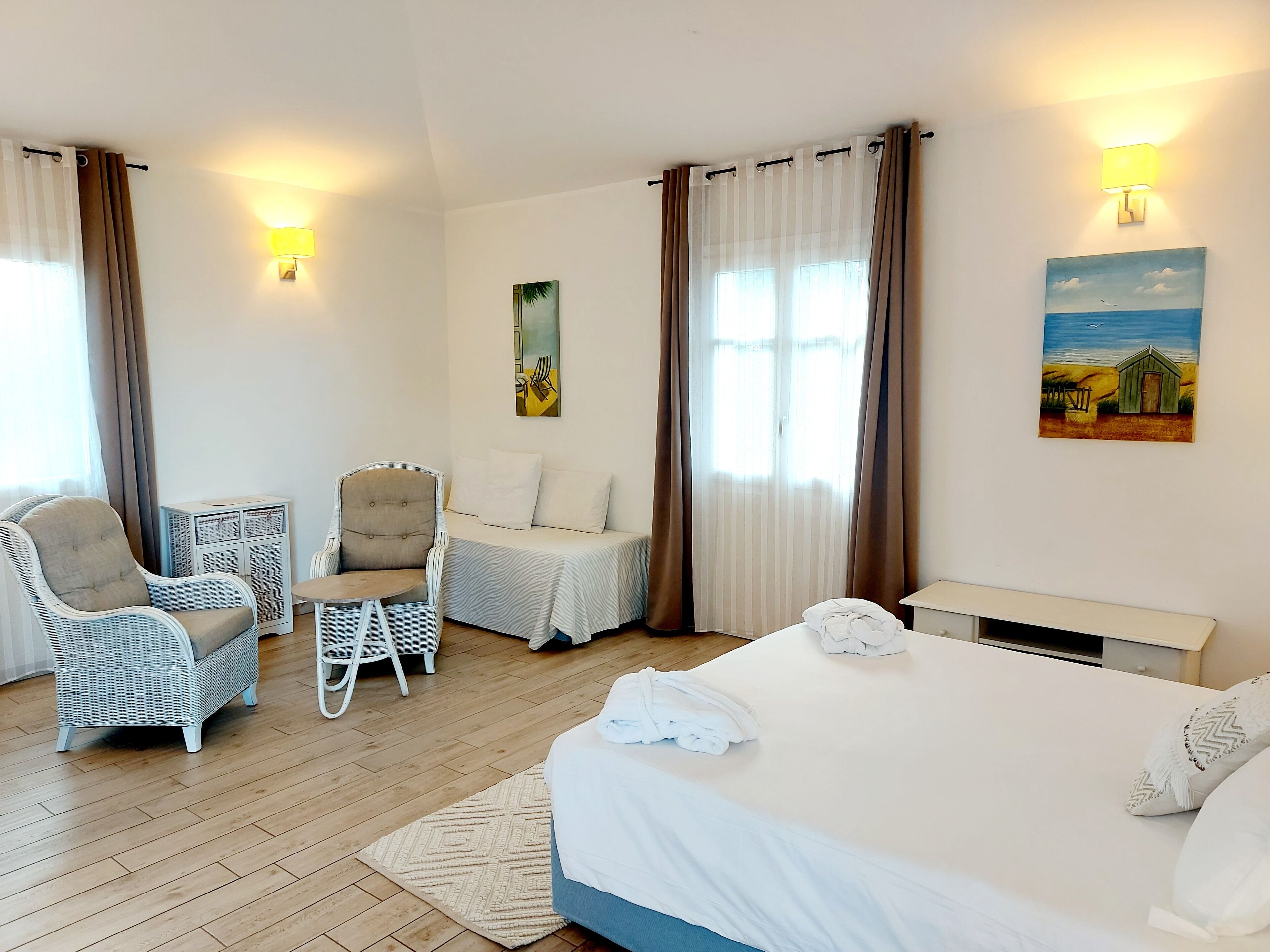 A hotel room with a bed, two chairs, a small table, a lamp, and a painting on the wall.