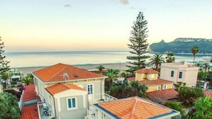 Una casa de dos pisos con tejado de tejas rojas, un balcón y vista al mar.