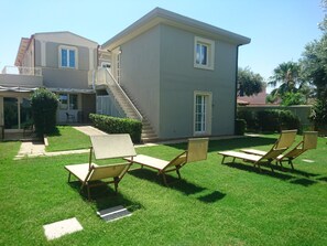 A two-story house with a covered patio area, a staircase, and a lawn with lounge chairs. - La Villa del Mare (Cagliari)
